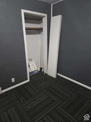 Room featuring charcoal-toned walls, patterned carpet tiles, and a closet with a built-in shelf