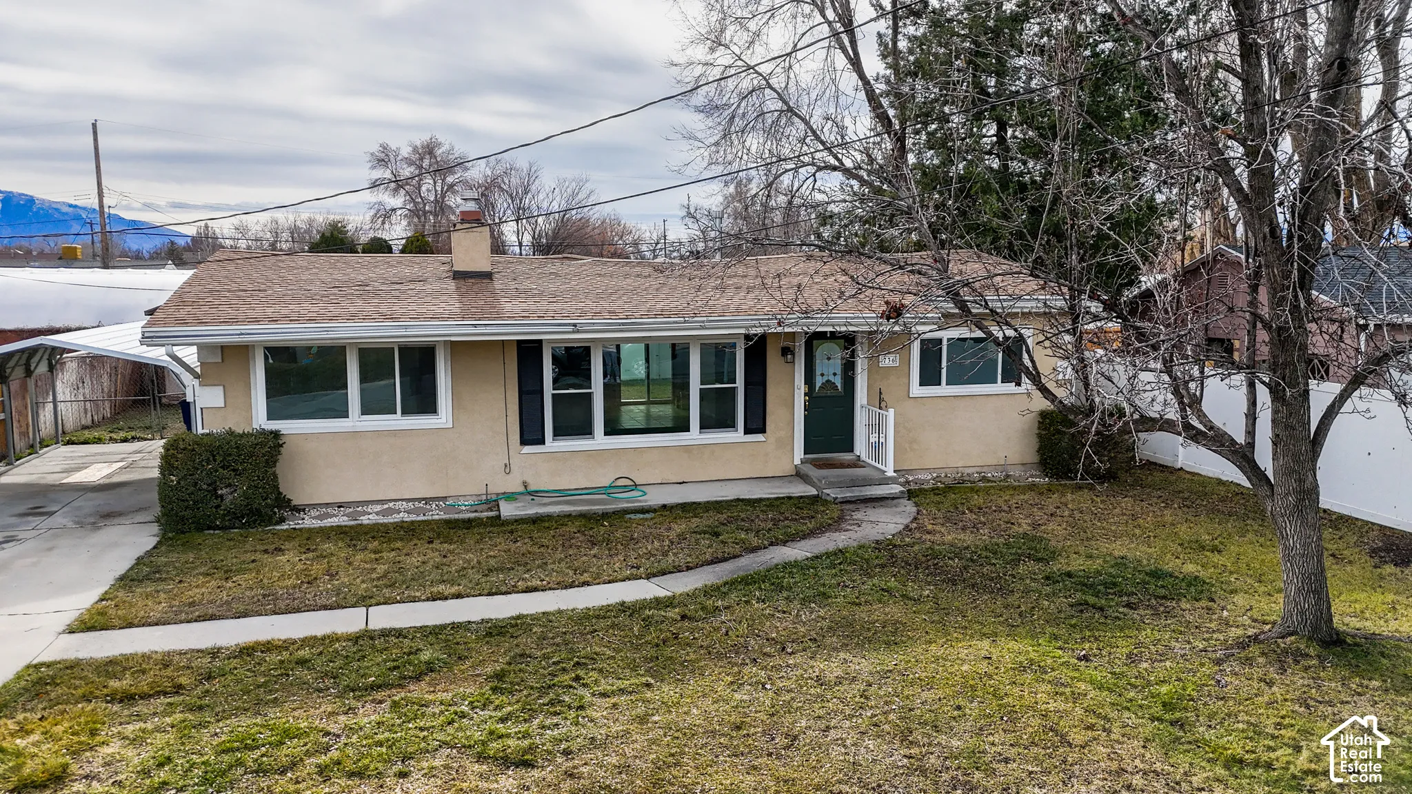 Single-story residence featuring a stucco exterior, shingled roof, attached carport, large windows with shutters, and mountain scenery