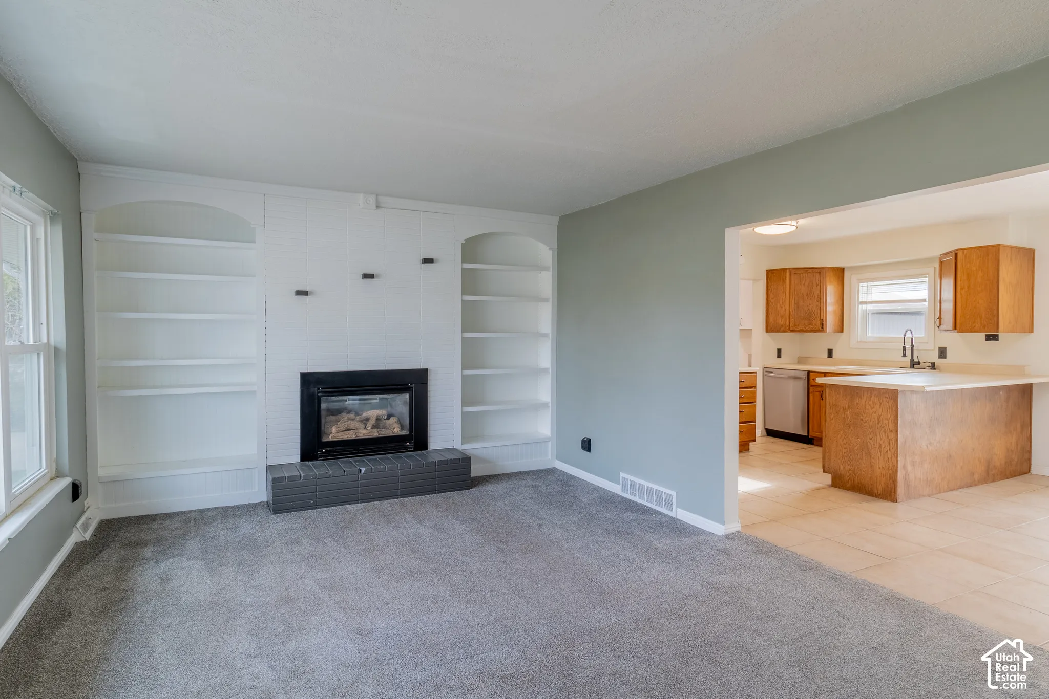 Living area featuring a fireplace with a masonry hearth and integrated white built-in shelving, complemented by tile flooring in the kitchen and cabinetry with integrated appliances