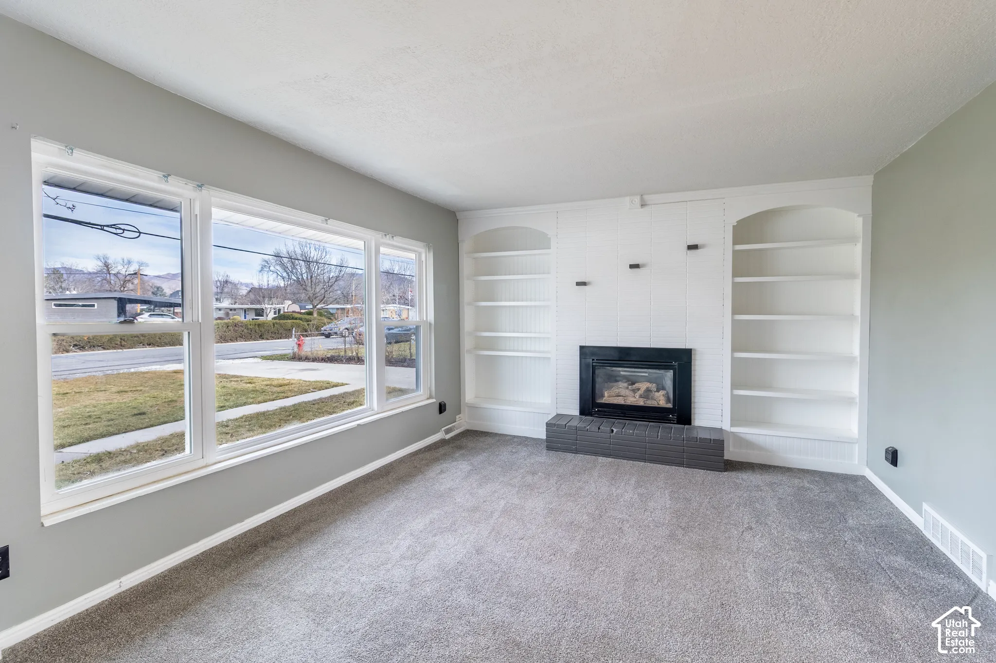 Living area featuring large windows, built-in shelving, and a fireplace with a masonry hearth