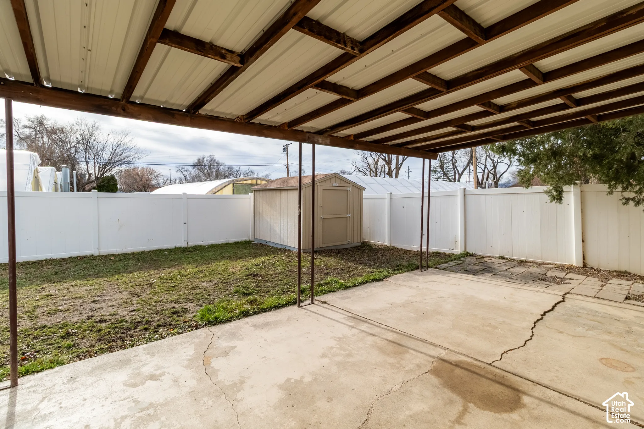 Covered patio with metal roofing and timber supports, concrete slab, vinyl privacy fencing, and detached storage shed