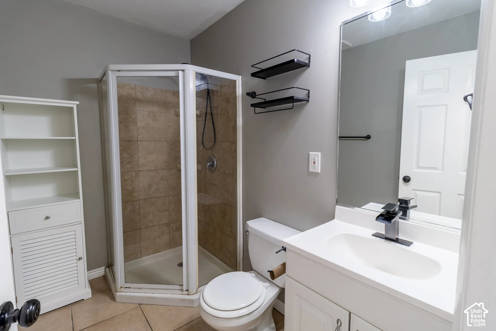 Bathroom featuring a white vanity with an integrated sink, a corner shower enclosure with tiled walls, built-in white cabinetry, a large wall-mounted mirror, and tile flooring
