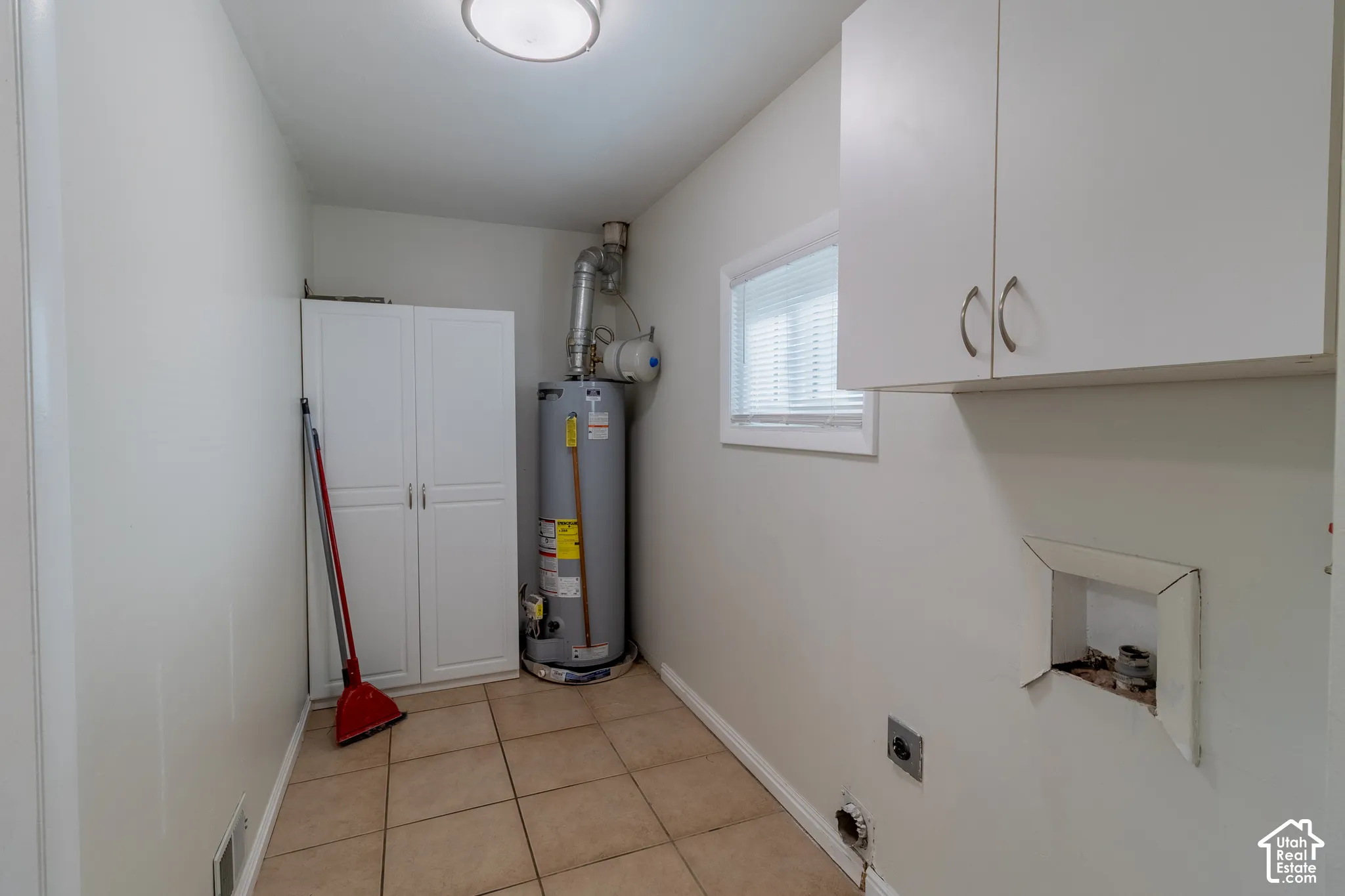 Utility area featuring ceramic tile flooring, white built-in storage cabinetry, wall-mounted upper cabinets, and a dedicated water heater
