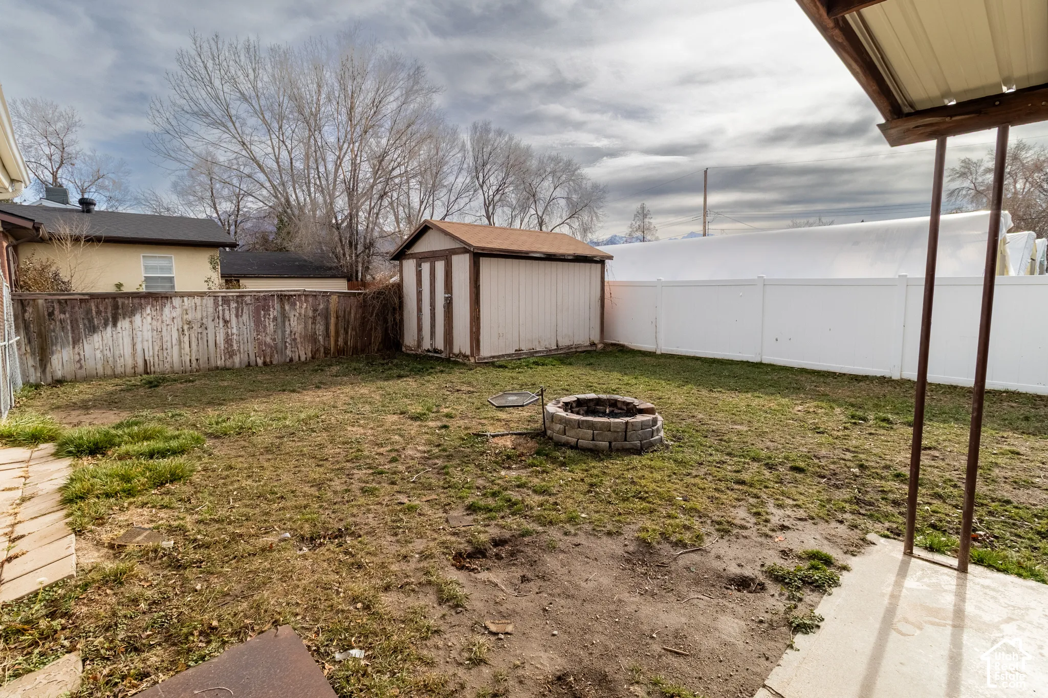 Backyard featuring a concrete patio, a stone fire pit, a detached storage shed, and a combination of wood and vinyl fencing