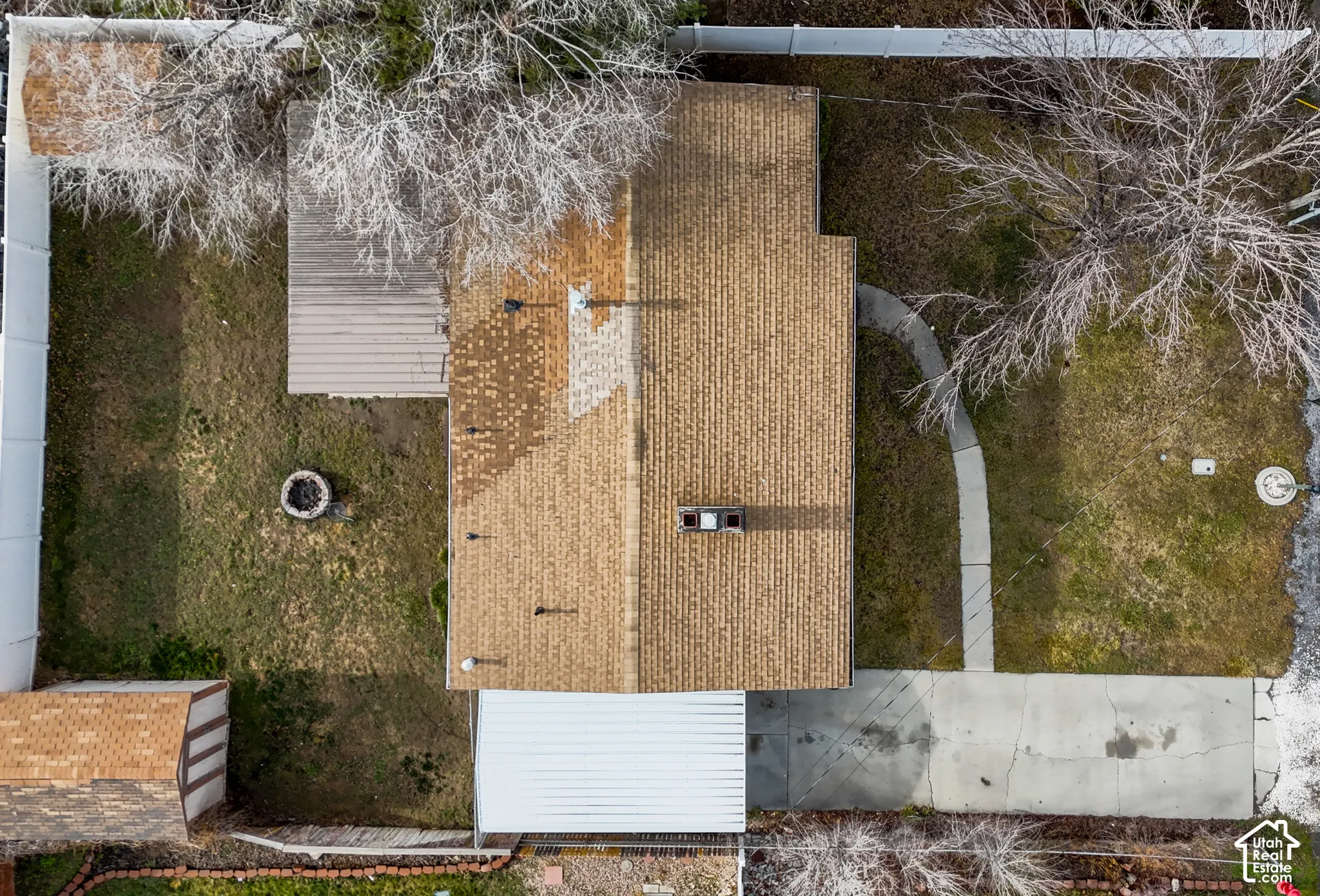 Aerial perspective featuring an asphalt shingle roof, a concrete driveway, a covered patio area, and a fenced yard with mature trees