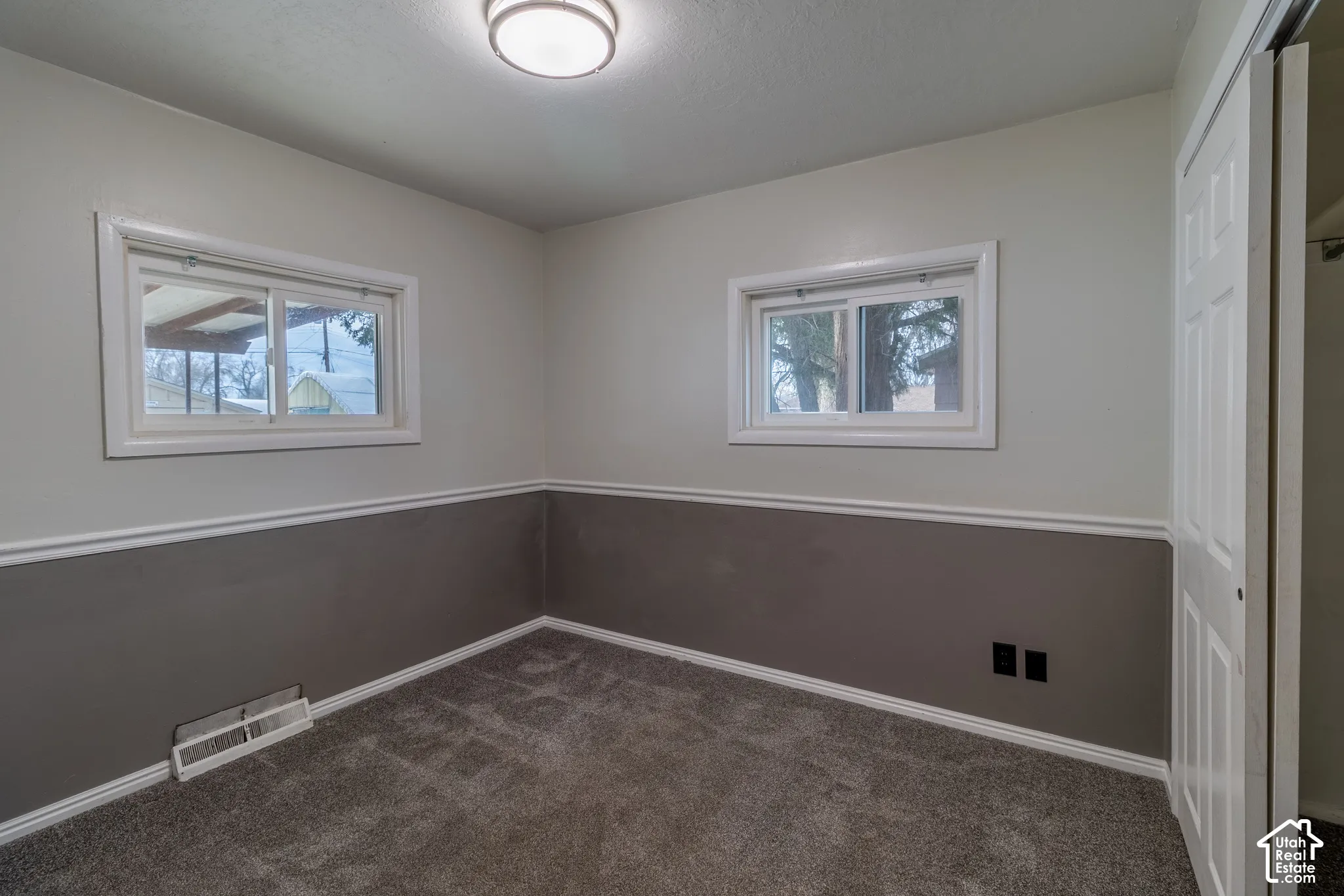 Interior space featuring two horizontal sliding windows, neutral two-tone wall paint with chair rail molding, carpeted flooring, and a flush-mount ceiling light