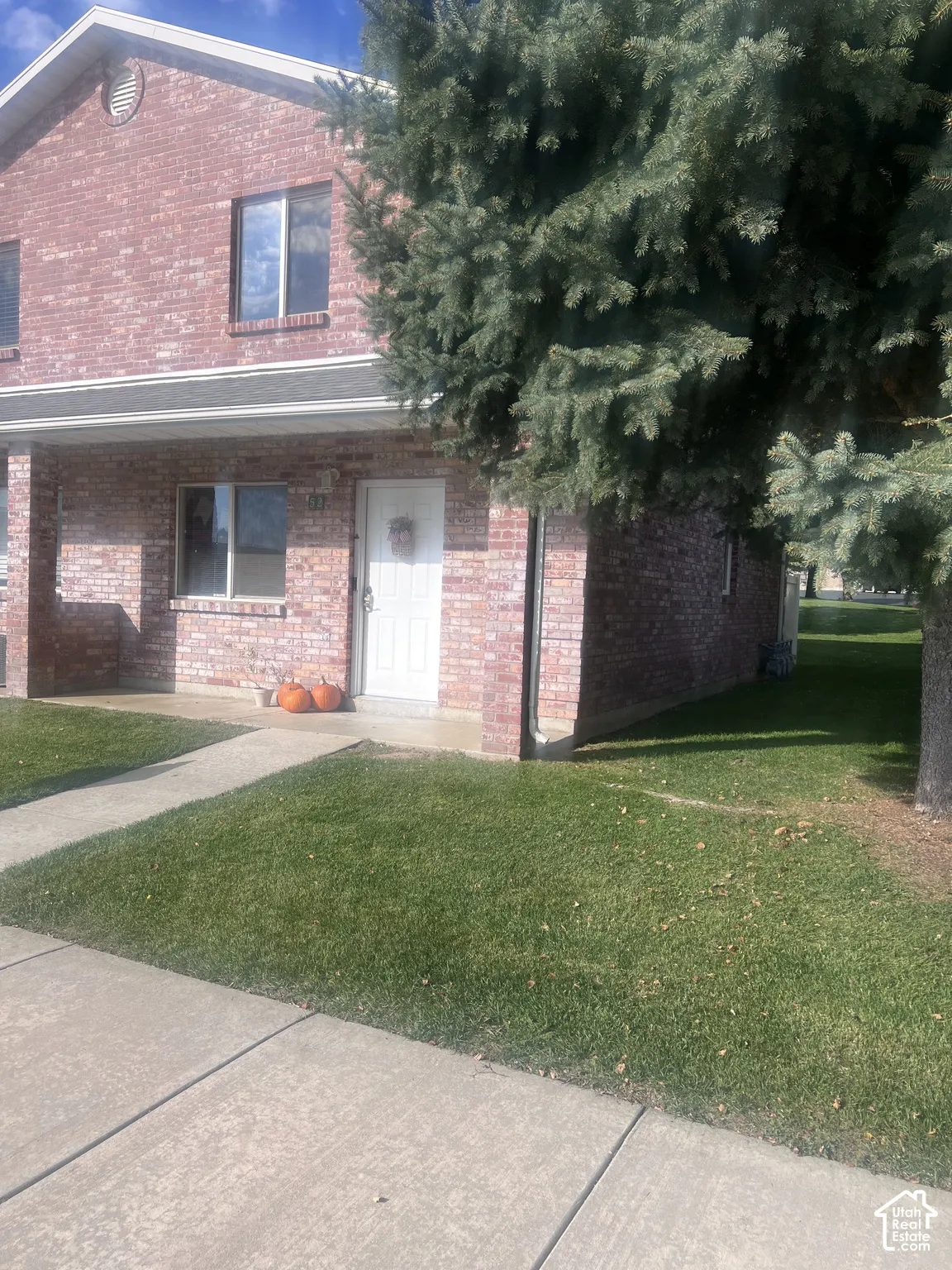 Two-story brick exterior featuring a covered front porch, concrete entryway path, and mature evergreen tree