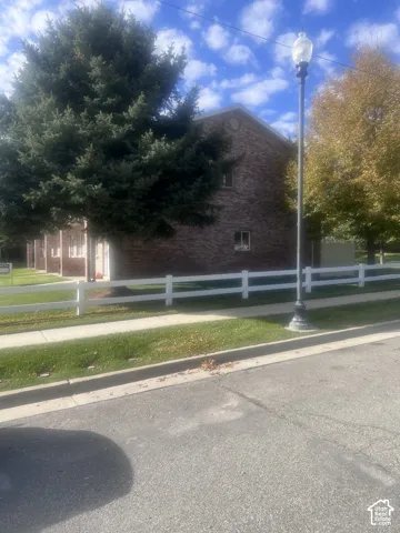 Brick exterior building with a white rail fence, mature trees, concrete sidewalk, and an outdoor light fixture