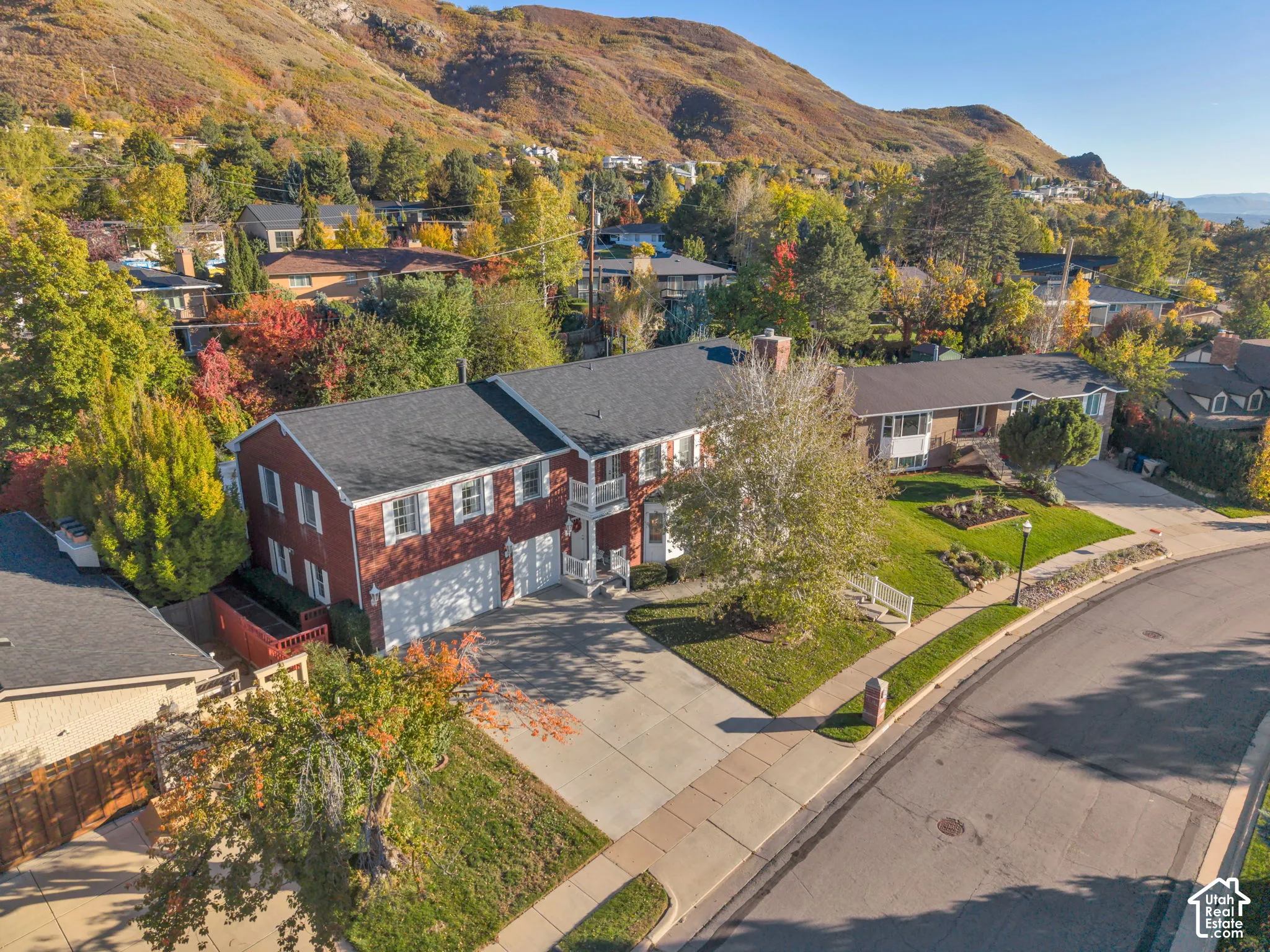 Two-story brick exterior featuring a multi-gabled roofline, an attached multi-car garage, white-trimmed windows, and a covered front entry, all situated against a hillside landscape
