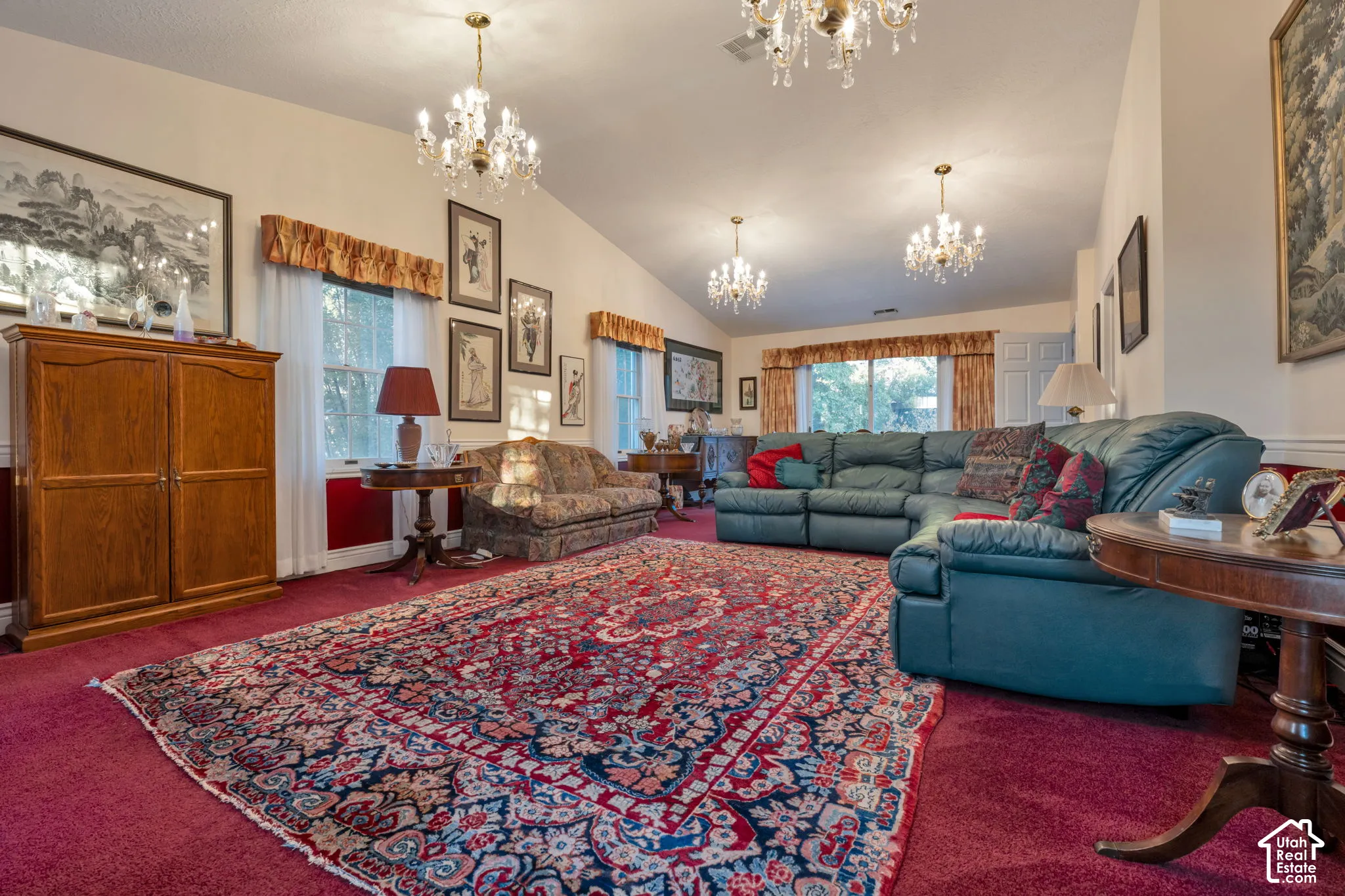 Living area featuring vaulted ceilings, multi-point crystal chandeliers, and multiple windows with cornice box valances