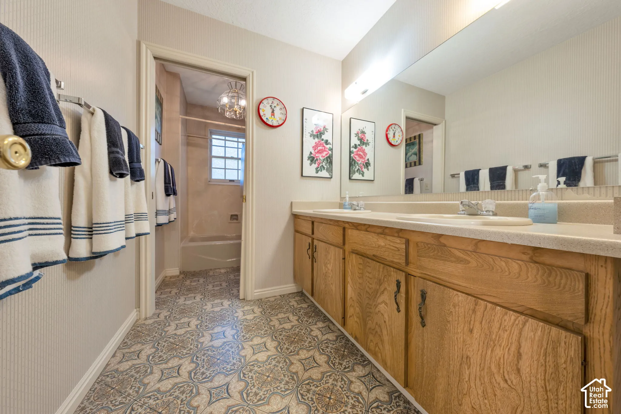 Bathroom featuring a dual-sink vanity with wood cabinetry, a large wall-mounted mirror, and a separate tub and shower enclosure