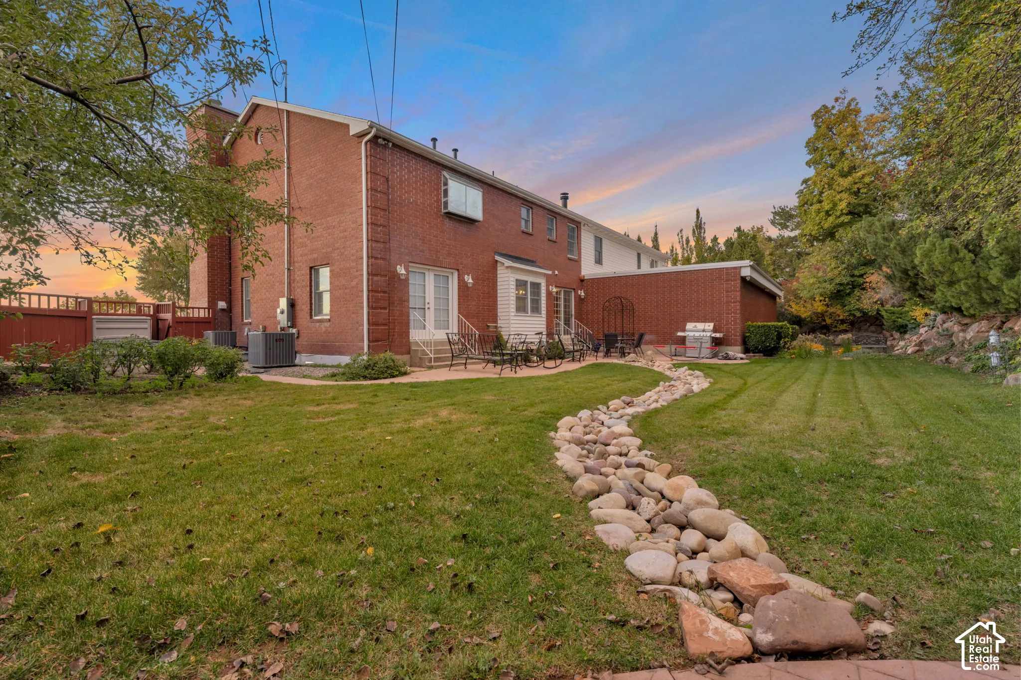 Backyard featuring a red brick exterior, a winding stone-lined dry creek bed, a paved patio, and mature trees