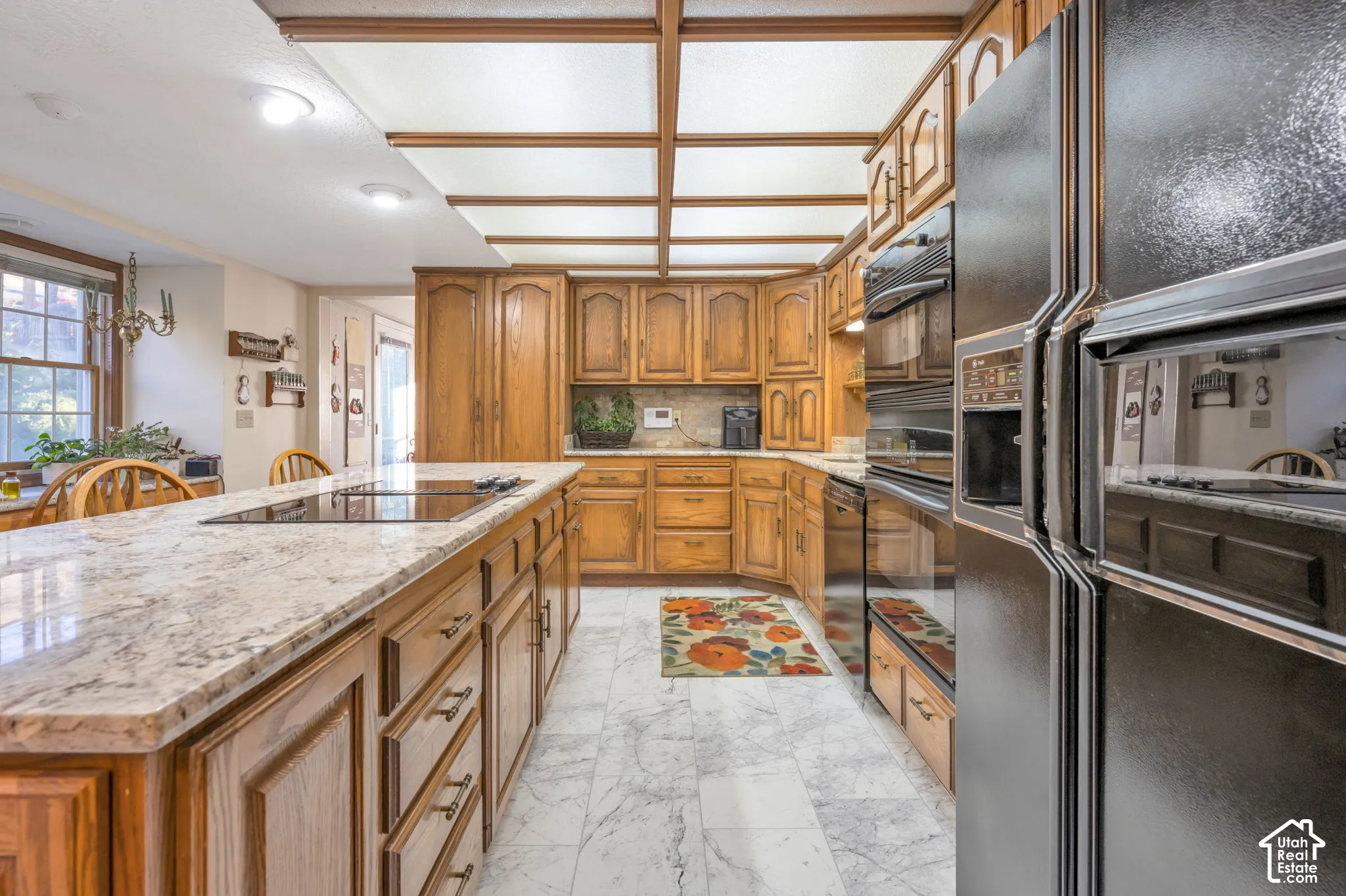 Kitchen featuring an expansive stone-topped island with a cooktop, stone-finish flooring, custom wood cabinetry, and built-in double wall ovens