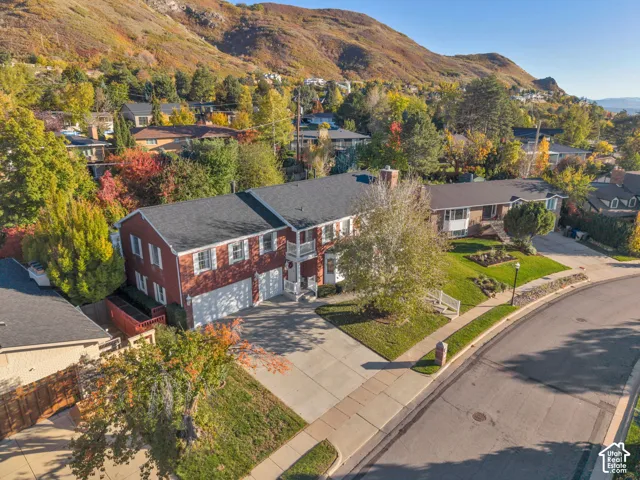 Two-story brick exterior featuring a multi-gabled roofline, an attached multi-car garage, white-trimmed windows, and a covered front entry, all situated against a hillside landscape
