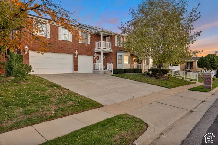 Red brick exterior featuring a three-car garage, white-trimmed windows, a multi-level balcony with white railings, and a heated concrete driveway