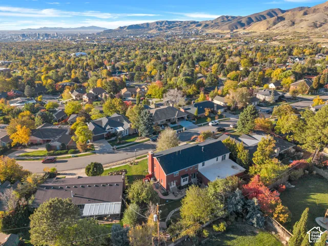 Aerial perspective featuring mature landscape, expansive residential lot, multi-level dwelling, and backdrop of mountain range and city skyline