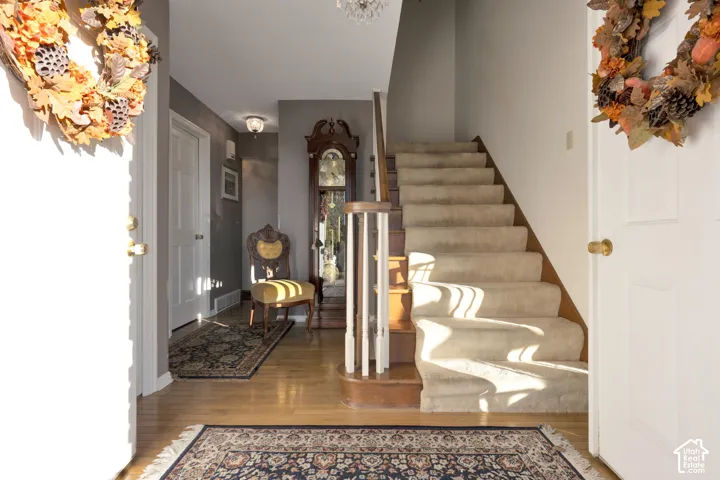 Foyer featuring wood flooring, carpeted staircase, wood-finish handrail, white painted balusters, coat closet