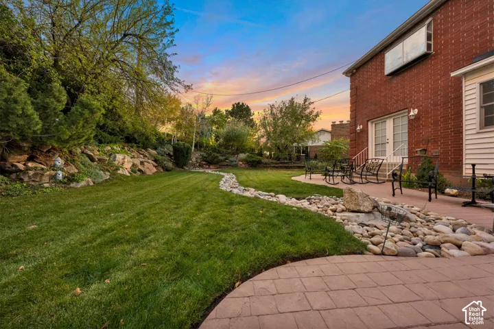 Backyard featuring a red brick exterior, stone retaining wall, paved patio, and rock-scaped garden bed