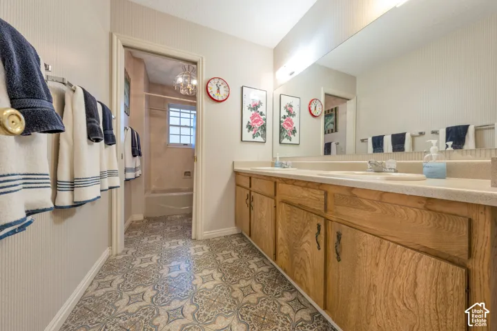 Bathroom featuring a dual-sink vanity with wood cabinetry, a large wall-mounted mirror, and a separate tub and shower enclosure