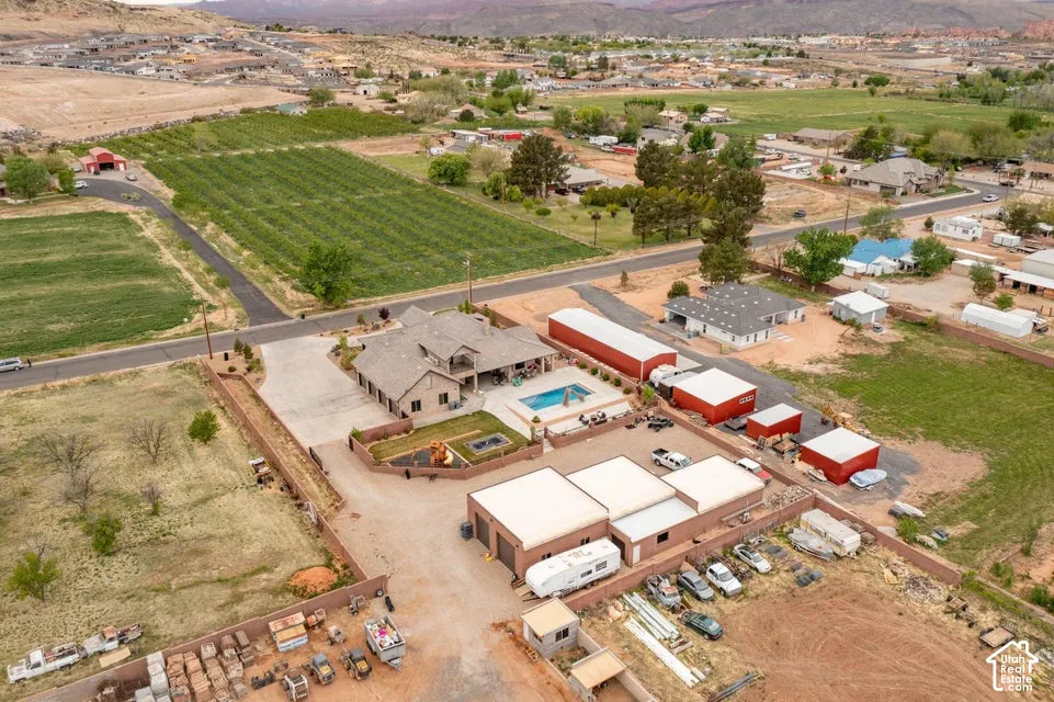Aerial perspective of a multi-structure compound featuring a swimming pool, integrated hardscaping, fenced grounds, and multiple outbuildings