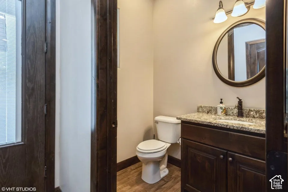 Bathroom featuring a stained wood vanity with a stone countertop, an undermount sink, a circular wall-mounted mirror, and wood-finish flooring