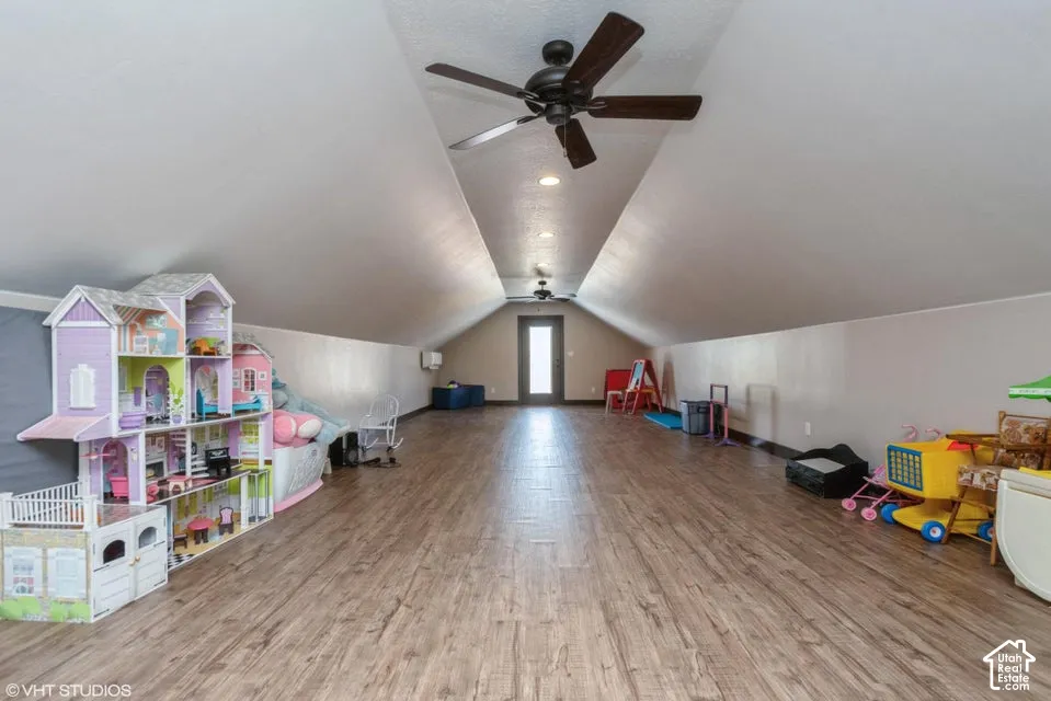 Vaulted ceiling with dual ceiling fans, wood-finish flooring, and exterior door with glass insert