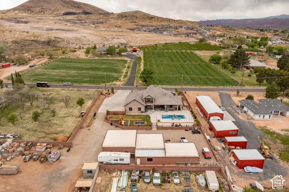 Aerial perspective featuring a multi-structure property with a primary residence, rectangular in-ground pool, fenced grounds, and mountain terrain backdrop