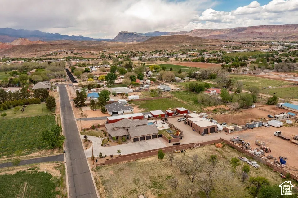 Aerial perspective featuring a multi-car garage, large storage structures, a concrete driveway, and an in-ground pool set against a mountain backdrop