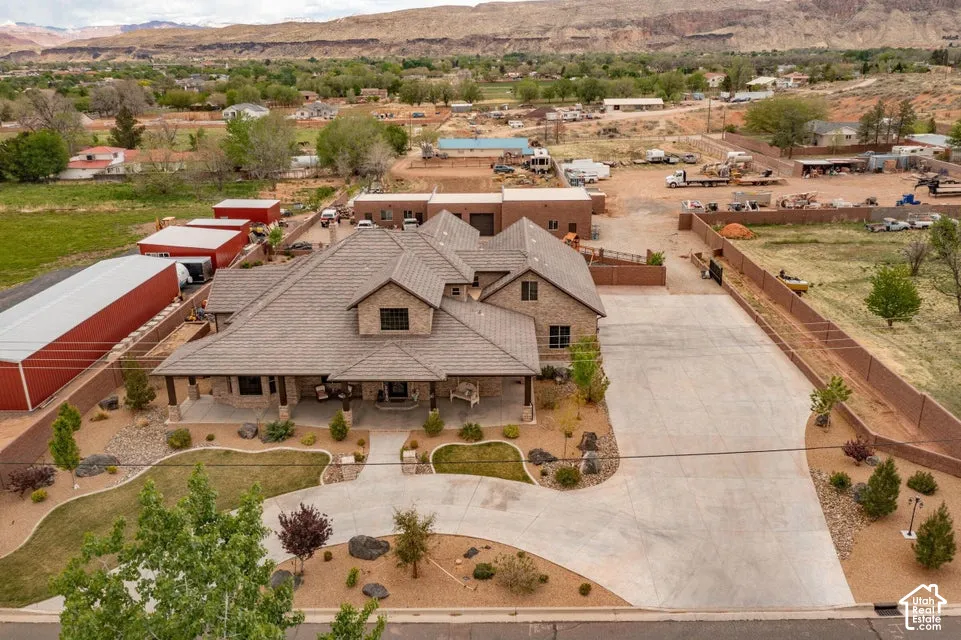 Multi-level brick exterior featuring a tiled roof, expansive concrete driveway, wrap-around covered front porch, and detached auxiliary storage structures