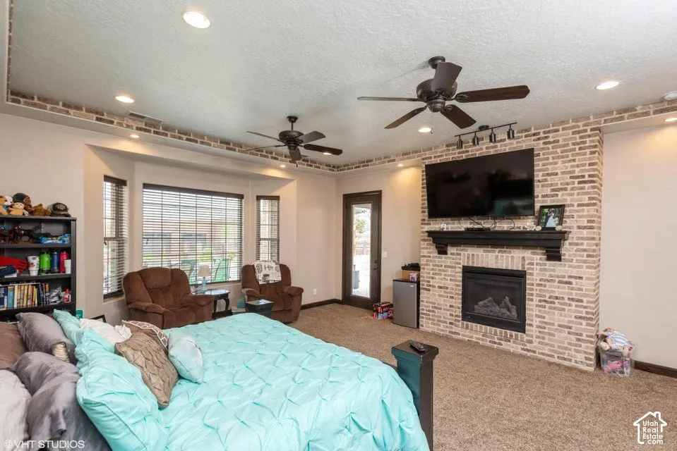Floor-to-ceiling brick fireplace with a custom mantel, recessed ceiling lighting, two dual-blade ceiling fans, and a tray ceiling featuring decorative brick inlay