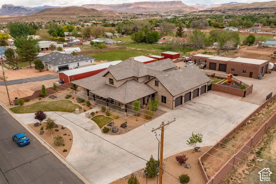 Multi-structure property featuring a primary residence with a tile roof, an expansive concrete driveway, a three-car garage, and a separate masonry outbuilding, set against a backdrop of desert mesas