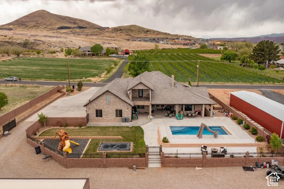 Brick exterior residence featuring a covered patio, swimming pool with an integrated slide, elevated masonry perimeter wall, and a large metal-sided outbuilding