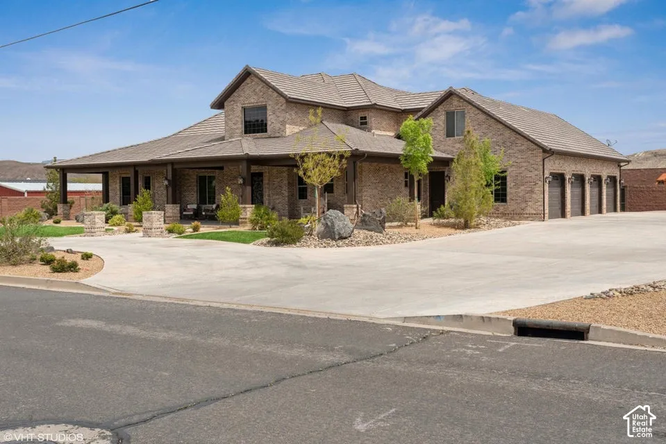 Custom brick exterior featuring a multi-gabled tile roof, an expansive covered porch, and a four-car attached garage