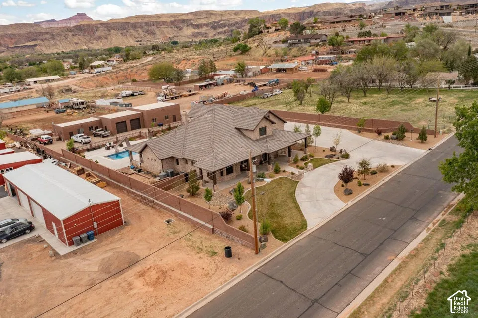 Multi-building property featuring a residence with a covered porch, a separate metal-sided outbuilding, a fenced swimming pool, and concrete driveway surfacing set against a desert mountain backdrop