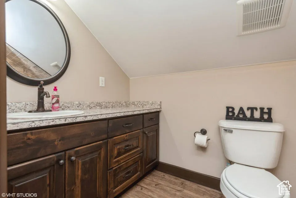 Dark-stained wooden cabinetry, light-toned stone-finish countertop with an integrated basin, round wall-mounted mirror, and wood-finish flooring