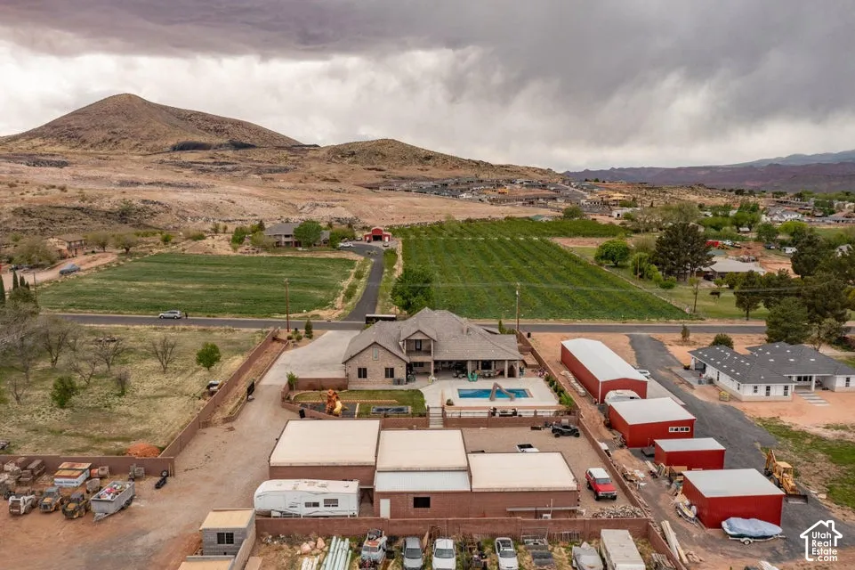 Aerial perspective featuring a multi-structure property with mountain terrain, an in-ground pool, expansive paved lot areas, and multiple detached outbuildings