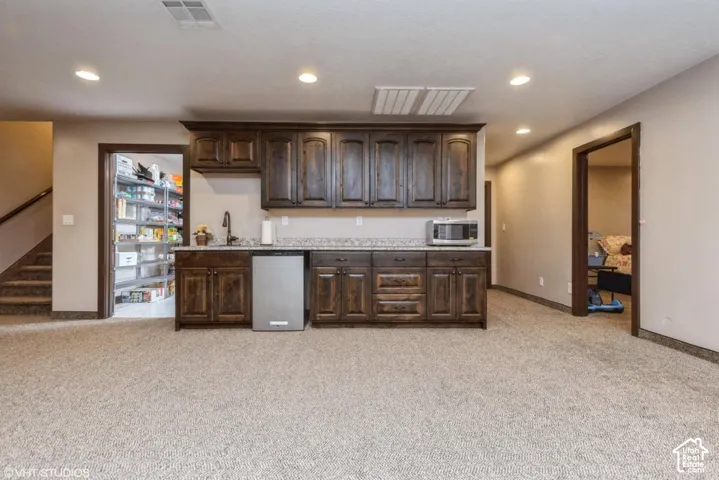 Wet bar featuring dark-stained wood cabinetry, stone-style countertops, an undermount sink with a gooseneck faucet, and recessed ceiling lighting