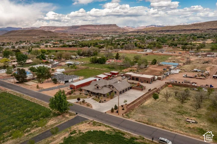 Aerial perspective of a multi-structure property featuring a residence, expansive concrete driveway, secondary detached garage, and metal-sided workshop, set against a backdrop of desert mesas