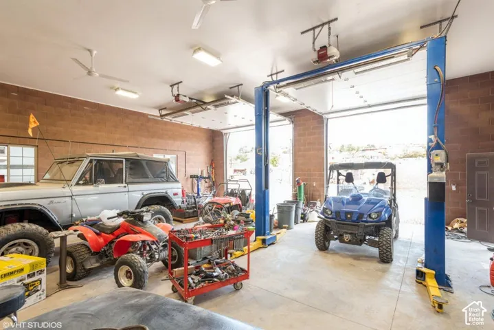 Spacious garage featuring concrete masonry unit walls, high ceilings with mounted lighting and fans, oversized garage doors, and an integrated vehicle lift