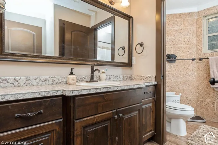 Bathroom vanity featuring dark-stained wood cabinetry, stone-patterned countertop, drop-in sink with oil-rubbed bronze faucet, oversized framed wall mirror, and textured masonry wall detailing