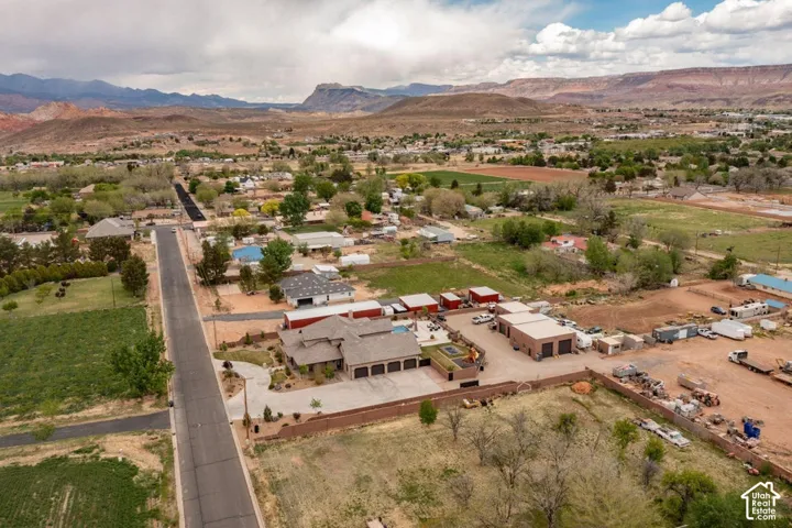 Aerial perspective featuring a multi-car garage, large storage structures, a concrete driveway, and an in-ground pool set against a mountain backdrop