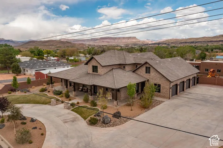 Brick exterior residence featuring a multi-gabled roofline, a wraparound covered porch, an attached four-car garage, and desert-inspired landscaping against a mountain backdrop
