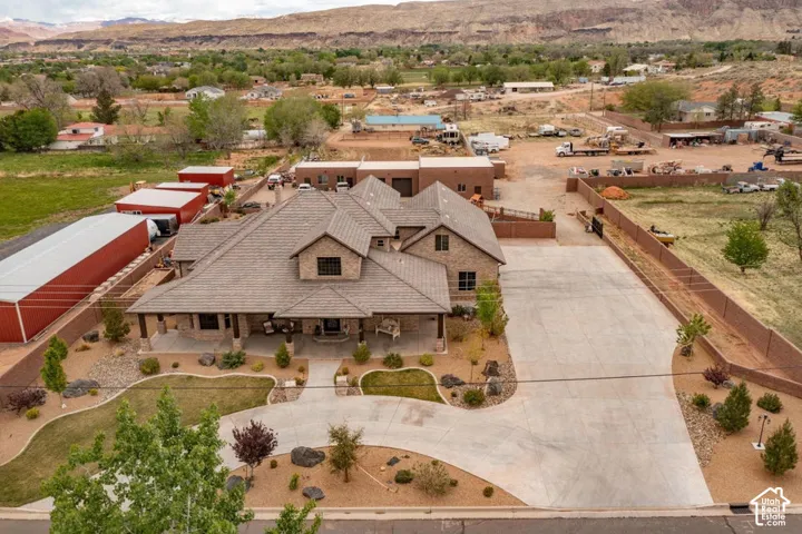 Multi-level brick exterior featuring a tiled roof, expansive concrete driveway, wrap-around covered front porch, and detached auxiliary storage structures