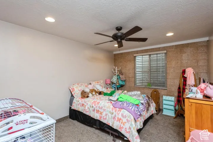 Textured masonry accent wall, recessed lighting, ceiling fan, and carpeted flooring