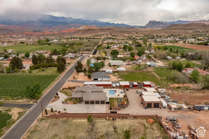 Aerial perspective featuring a multi-car garage, expansive concrete driveway, in-ground swimming pool, and multiple detached outbuildings, all set against a prominent mountain backdrop