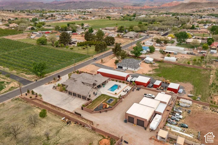 Aerial perspective featuring a multi-structure property with a private swimming pool, concrete driveway, stone-composite exterior, and multiple detached garage buildings