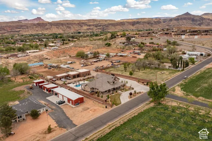 Aerial perspective featuring a multi-structure property with an inground pool, expansive detached garage facilities, concrete driveway, and surrounding mountain topography