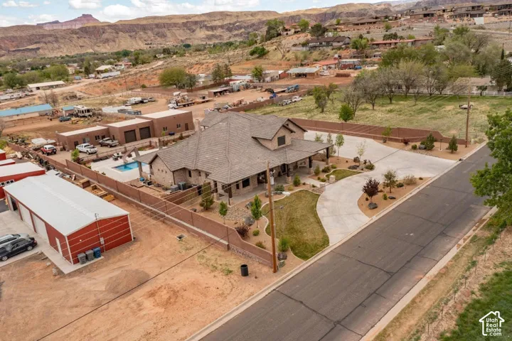 Multi-building property featuring a residence with a covered porch, a separate metal-sided outbuilding, a fenced swimming pool, and concrete driveway surfacing set against a desert mountain backdrop
