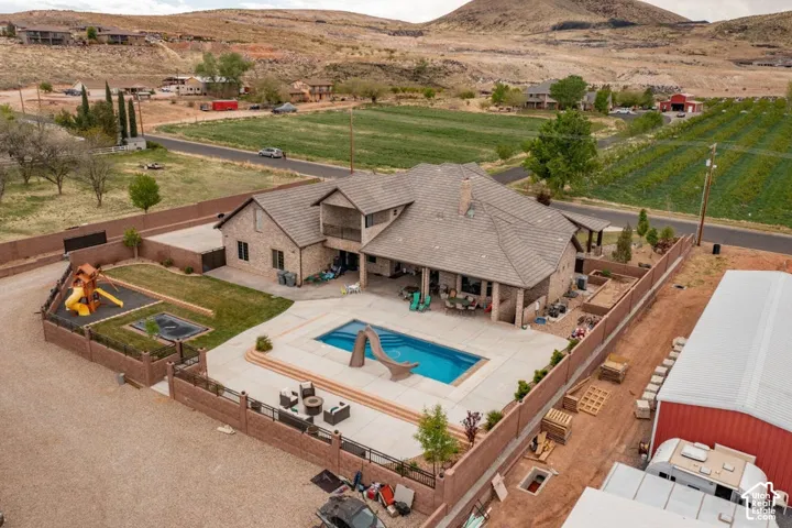Aerial perspective of a multi-level brick residence featuring a concrete-tiled roof, an inground swimming pool with a slide, a covered rear patio, and a fenced backyard area