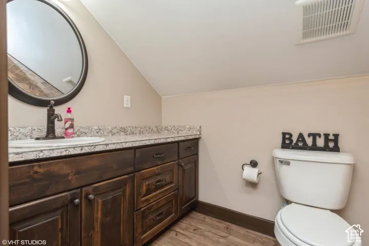 Dark-stained wooden cabinetry, light-toned stone-finish countertop with an integrated basin, round wall-mounted mirror, and wood-finish flooring
